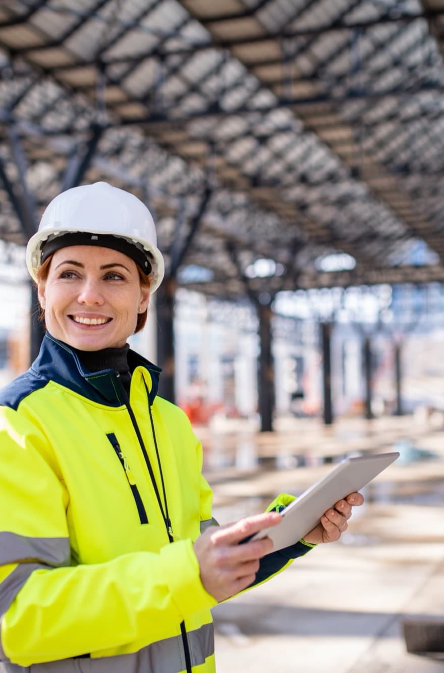 Smiling woman engineer holding a tablet beneath a steel roof structure