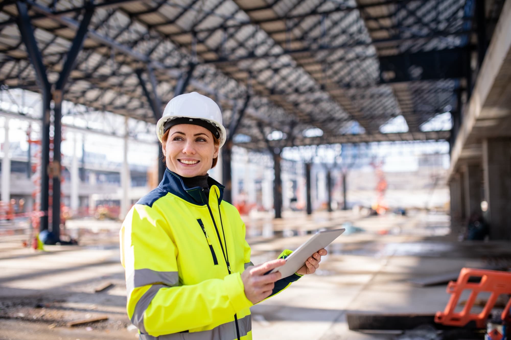 Smiling engineer reviewing estimate details on a tablet beneath a steel roof structure