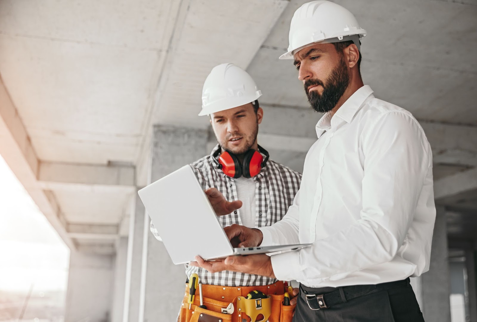 Two people at a construction site discuss some construction processes while looking at the data on a computer.